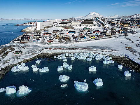 This file aerial view taken on March 11, 2025 shows icebergs floating in the waters beaten down by the sun with buildings in the background off Nuuk, Greenland, on the day of Greenland's legislative elections.