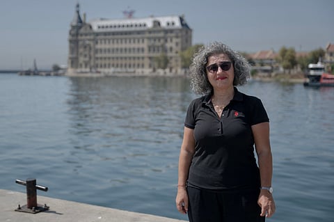 Turkish architect Gul Koksal poses during an interview with Haydarpasa train station in the background at Kadikoy in Istanbul, on August 22, 2025. Once immortalised in old Turkish films and portrayed in novels by famous Turkish authors, the station has recently been taken over by the culture ministry which wants to transform it into art centre. Perched on the waterfront, the picturesque railway station was inaugurated in 1908 at the end of the Ottoman Empire during the reign of Sultan Abdulhamid II as Europe
