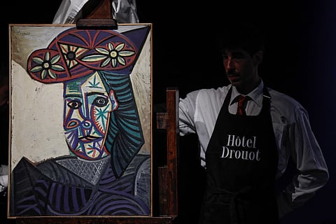 An employee unveals a painting by Spanish artist Pablo Picasso titled "Bust of a woman with a flowery hat."