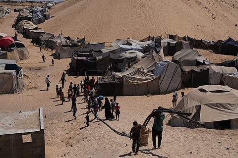 Displaced Palestinians walks through a tent camp in Muwasi, an area that Israel has designated as a safe zone, in Khan Younis, southern Gaza Strip, on September 21, 2025.