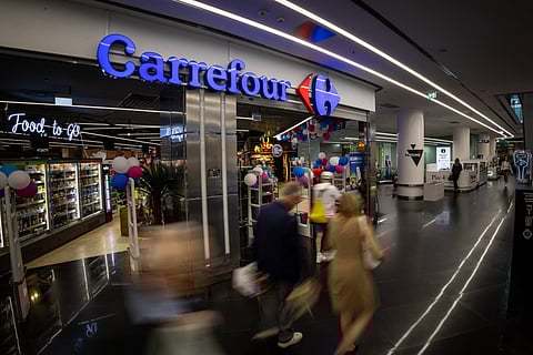 People pass-by the logo of the French supermarket chain Carrefour at the entrance to the store in a shopping mall on September 22, 2025.