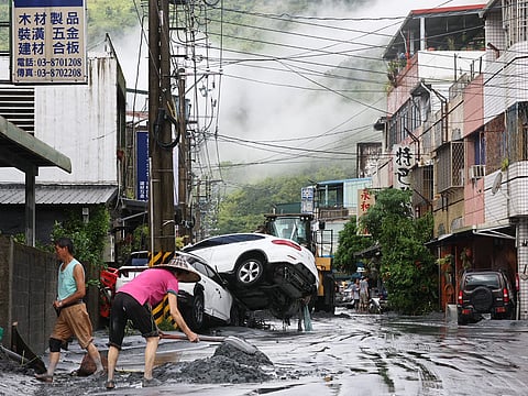 Residents clear mud from their property, while damaged cars are seen in the background, in Hualien.