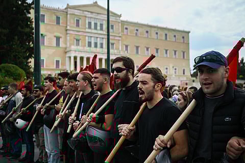 Protestors shout slogans as they gather near the Greek Parliament to take part in a demonstration during a 24-hour strike against government plans introducing an optional 13-hour workday, in Athens on October 14, 2025.