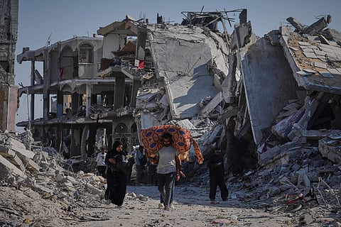 Palestinians walk among destroyed buildings in Gaza City,