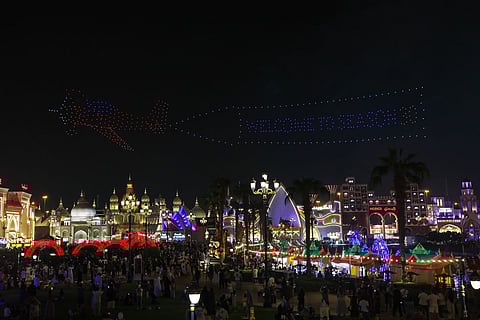 A vibrant evening at Global Village 2025 — visitors stroll past glowing food stalls serving Luqaimat, fries, and lobster rolls, with rides and pavilions lighting up the night sky.