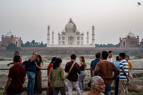 Tourists click photographs with the backdrop of the Taj Mahal in Agra on October 17, 2025.