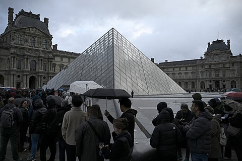 People queue in the Louvre pyramid courtyard moments before the announcement the museum will remain closed for a second day running after thieves stole crown jewels from the museum in Paris a day earlier, in Paris on October 20, 2025.