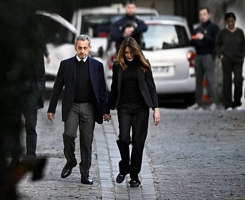 France's former president Nicolas Sarkozy (L), with his wife Carla Bruni-Sarkozy, leaves his residence to present himself to La Sante Prison for incarceration on a five-year prison sentence after being convicted of criminal conspiracy over a plan for late Libyan dictator Muammar Gaddafi to fund his 2007 electoral campaign, in Paris, on October 21, 2025.