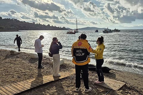 This handout photograph taken and released on October 24, 2025 by Turkish news agency DHA (Demiroren News Agency) shows emergency officials standing next to the body of a migrant as Turkish coastguard boats (background) search for victims off the coast of Bodrum, following the capsize of a dinghy in the Aegean Sea.