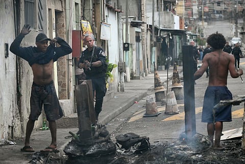 A police officer holds his gun up next to residents on a barricade during the Operacao Contencao (Operation Containment) at the Vila Cruzeiro favela, in the Penha complex, in Rio de Janeiro, Brazil, on October 28, 2025.