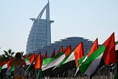 A woman stabds next to a flag garden in the colours of the United Arab Emirates set up along the beach with Dubai's landmark Burj al-Arab luxury hotel in the background, two days ahead of the annual UAE Flag Day celebrations on November 1, 2025.