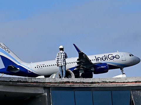 A man stands atop an under-construction building as an Indigo aircraft prepares to land at Kempegowda International Airport in Bengaluru on December 4, 2025.