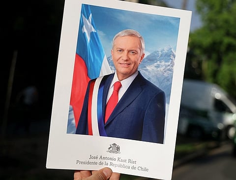 A person shows a sign depicting Chile's presidential candidate Jose Antonio Kast, of the Partido Republicano party, that reads his name and "President of the Republic of Chile", following the first results of the presidential runoff election in Santiago on December 14, 2025.