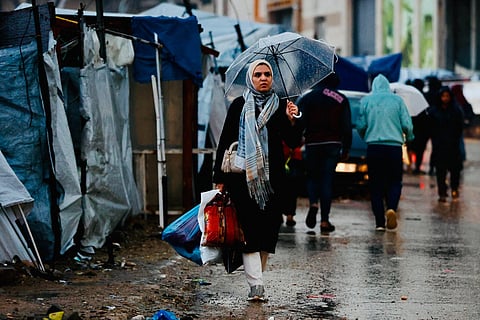 A displaced Palestinian woman holds an umbrella to shield from the rain in Gaza City on December 15, 2025.