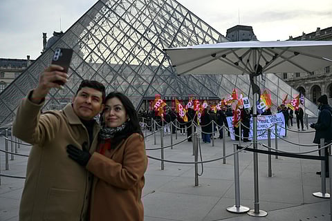 A couple take a selfie outside the closed Louvre Museum as museum workers strike against increasingly deteriorating working conditions and the declining visitor experience at the world famous museum, in Paris on December 15, 2025.
