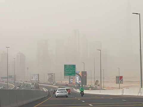 Motorists drive amid dusty weather conditions with Dubai’s skyline in the background.