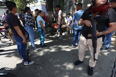 An armed supporter of ousted Venezuelan President Nicolas Maduro stands guard as he monitors vendors from speculating on goods prices in Caracas on January 4, 2026, one day after he was captured in a U.S. raid.