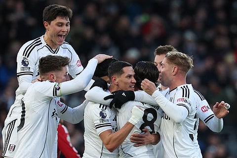 Fulham's Welsh midfielder #08 Harry Wilson (C) is mobbed by teammates after scoring the opening goal to take the lead 1-0 during the English Premier League football match between Fulham and Liverpool at Craven Cottage in London on January 4, 2026.