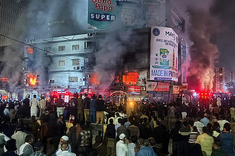 People gather as firefighters try to control a massive fire that broke out in a multi-story shopping mall, in Karachi on January 17, 2026.