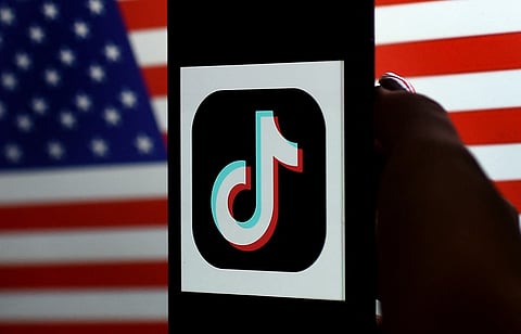 Photo illustration shows the TikTok logo displayed on the screen of an iPhone on a US flag background.