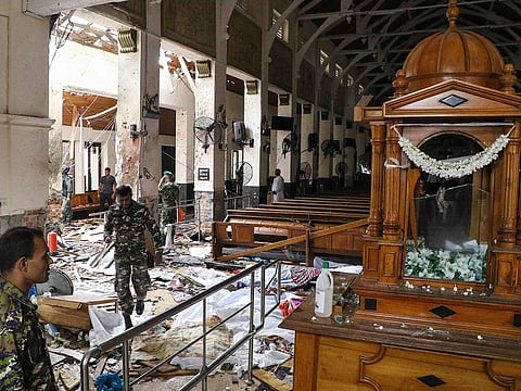 Sri Lankan security personnel walk past dead bodies covered with blankets amid blast debris at St. Anthony's Shrine following an explosion in the church in Kochchikade in Colombo on April 21, 2019.