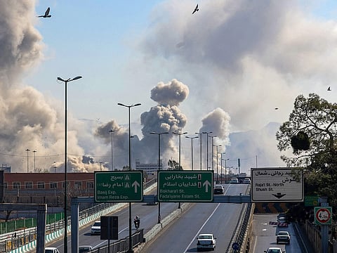 Motorists drive along an expressway as plumes of smoke rise after a strike in Tehran.