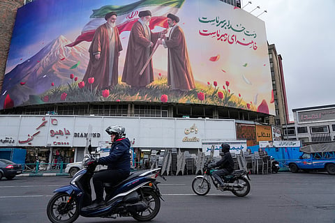 Motorbikes drive past a billboard depicting Iran’s late Supreme Leader Ayatollah Ali Khamenei, center, handing the country’s flag to his son and successor Ayatollah Mojtaba Khamenei, right, as the late revolutionary founder Ayatollah Ruhollah Khomeini stands at left, in a square in downtown Tehran, Iran, Tuesday, March 10, 2026.