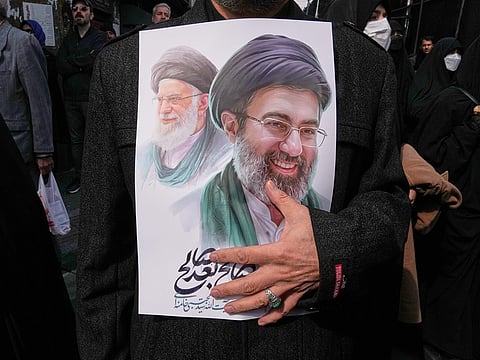 A mourner holds a poster depicting Ayatollah Mojtaba Khamenei, right, the successor to his late father Ayatollah Ali Khamenei, left, as supreme leader, during the funeral procession for senior Iranian military officials and civilians killed during the US-Israel campaign in Tehran, Iran, Wednesday, March 11, 2026.