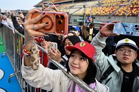 Fans watch Ferrari's team members during pit stop practice ahead of the Formula One Chinese Grand Prix at the Shanghai International Circuit in Shanghai on March 12, 2026.