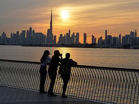 A family enjoys the sunset with the view of the city skyline and Burj Khalifa, in Dubai.