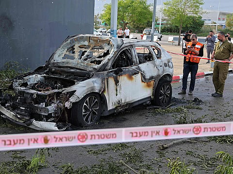 An Israeli security personnel and a first responder inspect the site of an Iranian strike that hit a car in Petah Tikva on March 18, 2026.