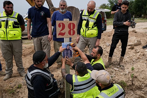 Paramedics attach a portrait over the grave of Ghadir Baalbaki, 19, who was killed on Tuesday in an Israeli airstrike, at a temporary mass grave in the southern port city of Tyre, Lebanon, Wednesday, April 15, 2026.