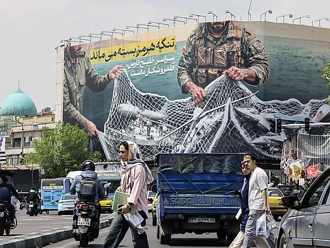 Iranian walks past a giant billboard reading 'The Strait of Hormuz remains closed' at the Revolution Square in Tehran, amid a ceasefire in the region.