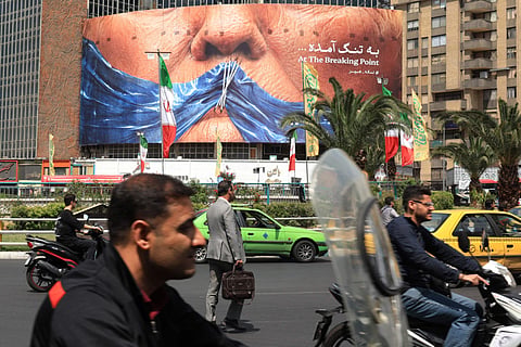 Commuters make their way past an anti-US billboard referring to President Donald Trump and the Strait of Hormuz, installed on a building at the Valiasr Square in Tehran on May 2, 2026.