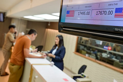 A monitor displays the selling and buying exchange rates of the Rupiah against the US Dollars, as a money changer serves a customer (back) in Jakarta on May 12, 2026, amid the Rupiah's depreciation against the USD. (Photo by BAY ISMOYO / AFP)