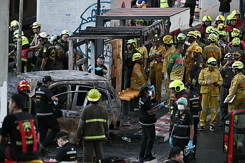 Forensic police officers, rescue workers and firefighters stand at the site of a train collision with a bus underneath Makkasan Airport Rail station in Bangkok on May 16, 2026.