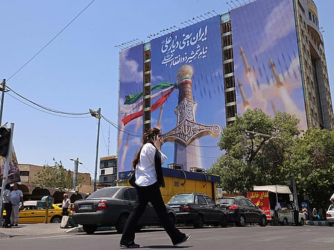 A woman walks past a giant banner depicting Iranian missiles and a sword belonging to Imam Ali, the first Imam of the Shiites, at the Vanak Square in Tehran.