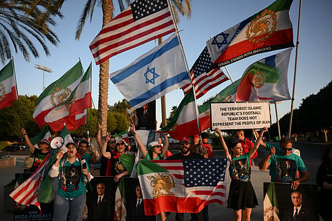 People hold pre-revolutionary Iranian flags as they protest the Iranian regime outside Carson Sports Park before Iran’s training session in Los Angeles on June 14, 2026, on the eve of the 2026 World Cup football match between Iran and New Zealand.