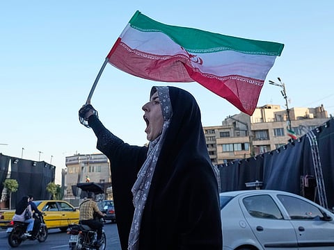 A woman waves an Iranian flags as she chants slogans against Iran and US talks at the Islamic Revolution square in Tehran, Iran, Sunday, June 14, 2026.