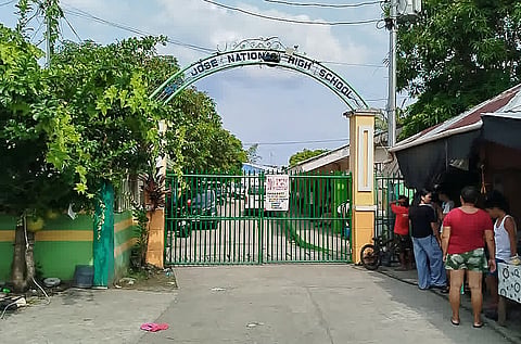 People stand next to the entrance gate of San Jose National High School after a shooting incident in Tacloban City, Leyte province on June 22, 2026.