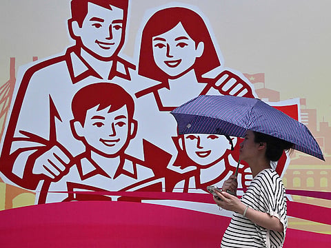 A woman holding an umbrella walking past a billboard of a happy family in Hanoi.