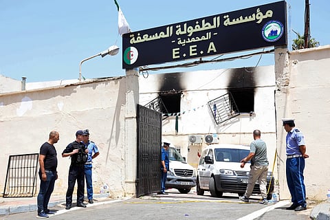 Police officers stand guard as vehicles leave through the entrance of an orphanage following a fire in the Mohammadia suburb of Algiers on July 16, 2026.