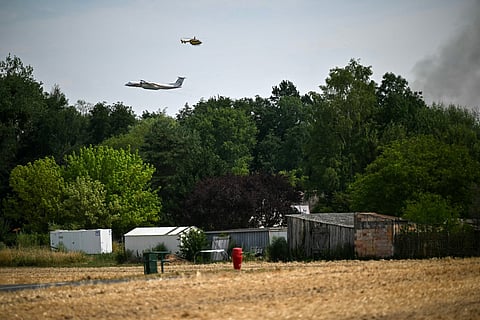 This photograph shows a Dash 8-Q400MR aircraft of the civil security and a firefighter helicopter operating near a plume of smoke from a fire in the Fontainebleau Forest, in Noisy-sur-Ecole, in the Paris' Ile-de-France region on July 16, 2026.