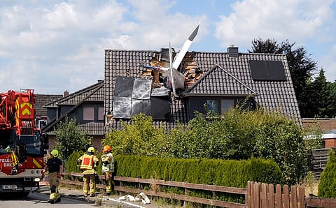 The tail of an airplane protrudes from the roof of a residential building after a crash as firefighters are at work.