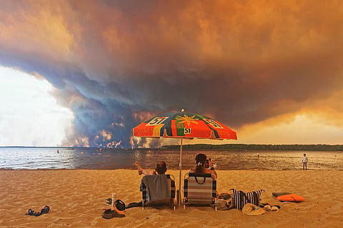 Beach goers sit on the beach of Moutchic in Lacanau, France on July 24, as clouds of smoke rise into the sky from a wildfire. Authorities urge tourists to avoid blaze-hit regions but stop short of bans