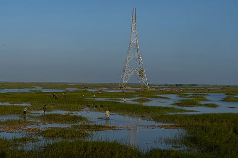 Workers walk through a swamp to install electric transmission towers for the Adani Renewable Energy Park near Khavda, Bhuj district, near the India-Pakistan border in the western state of Gujarat, India, Sept. 21, 2023.