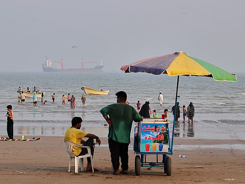 A juice seller serves beachgoers from his cart as commercial vessels sit anchored in the Strait of Hormuz off Bandar Abbas, Iran.