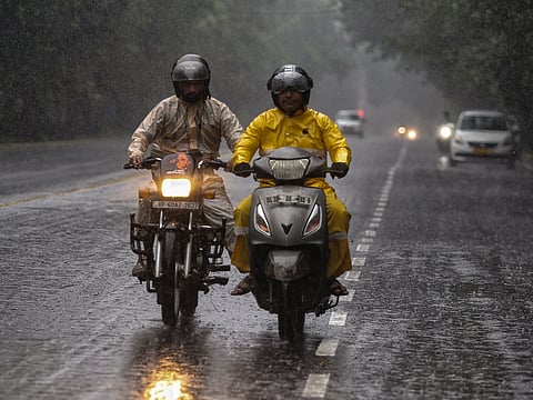 Commuters on two-wheelers make way through a rain-slicked road amid rainfall, in New Delhi on Saturday.