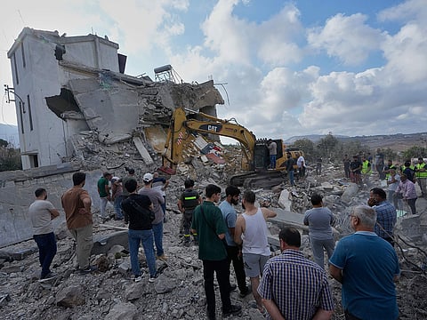 People watch rescue workers use an excavator as they conduct a search operation at a destroyed house that was hit by an Israeli airstrike in Arab Salim village, southern Lebanon.