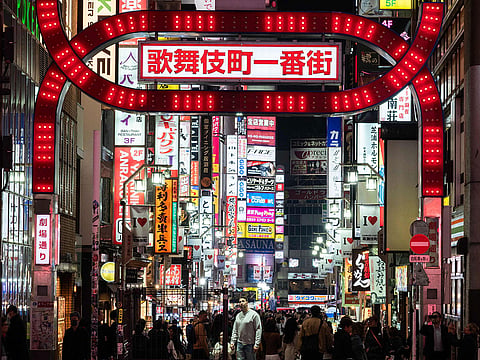A man is illuminated as he looks up at a large neon sign in the Shinjuku district in Tokyo.